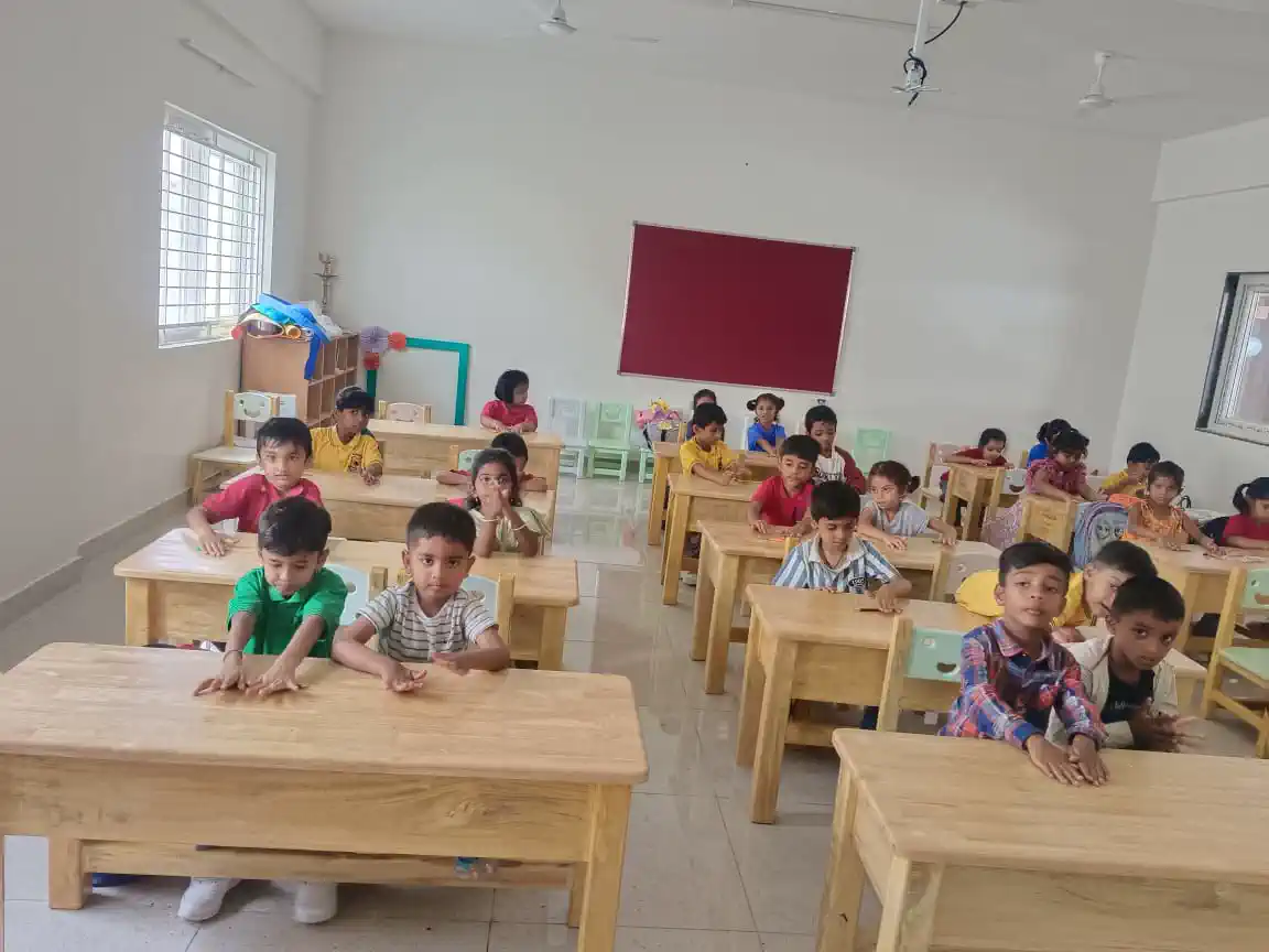 Pre-school children seated at wooden desks in a bright classroom at Takshashila School @ Rampura